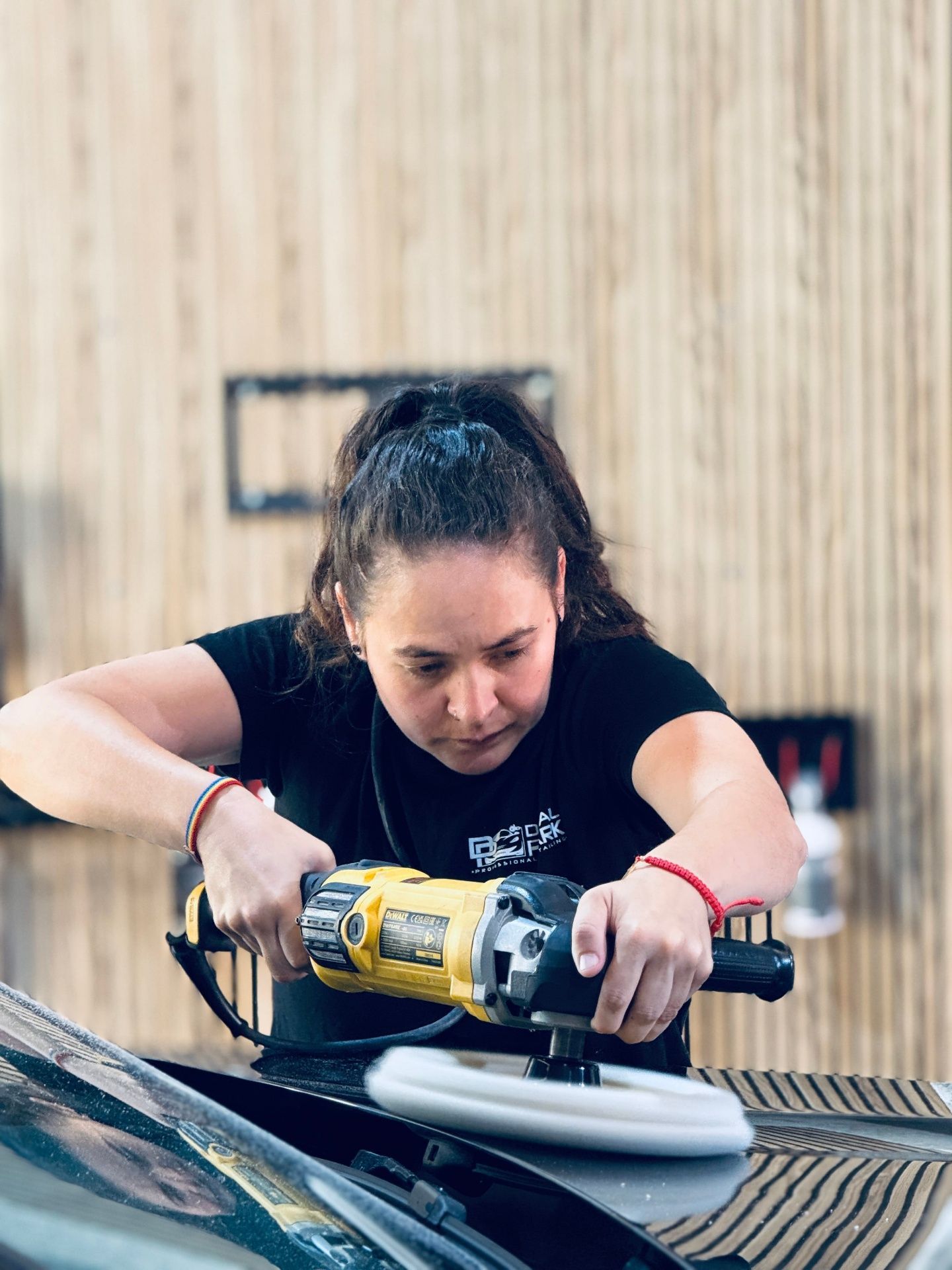 Alumna concentrada puliendo carrocería con pulidora DeWalt profesional durante formación en Detail Park
