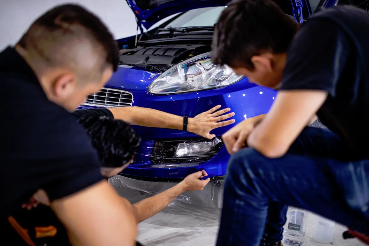 Alumnos instalando film de protección de pintura en el frontal de un coche azul