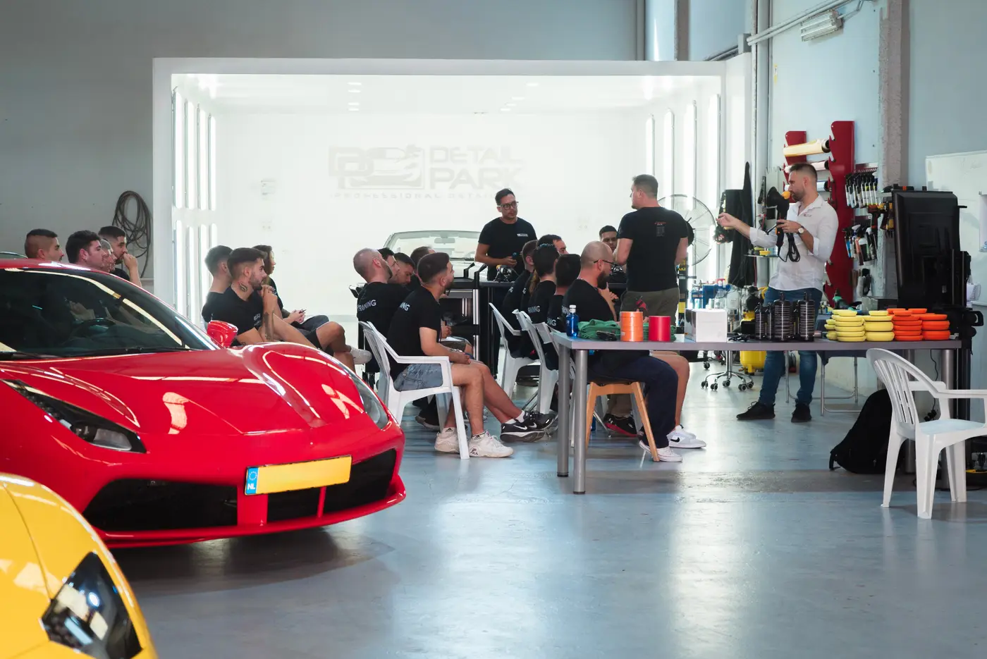 Nave de Detail Park con alumnos atendiendo una explicación junto a un Ferrari rojo