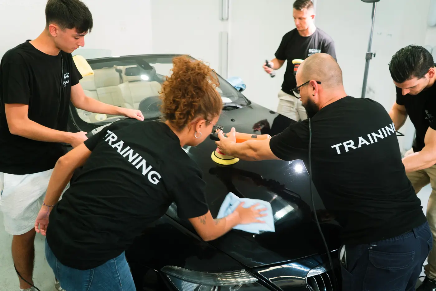 Alumnos con camiseta de la academia puliendo juntos un coche negro